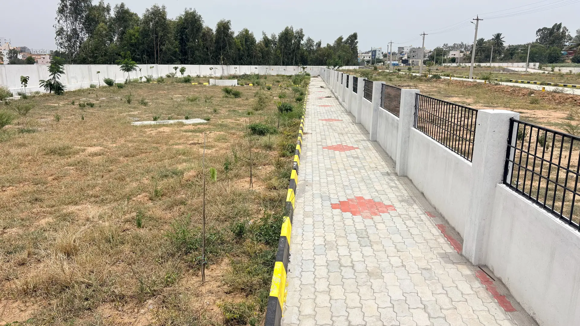 Paver walkway and finished compound wall running between marked plots at Poes Garden, Hosur.